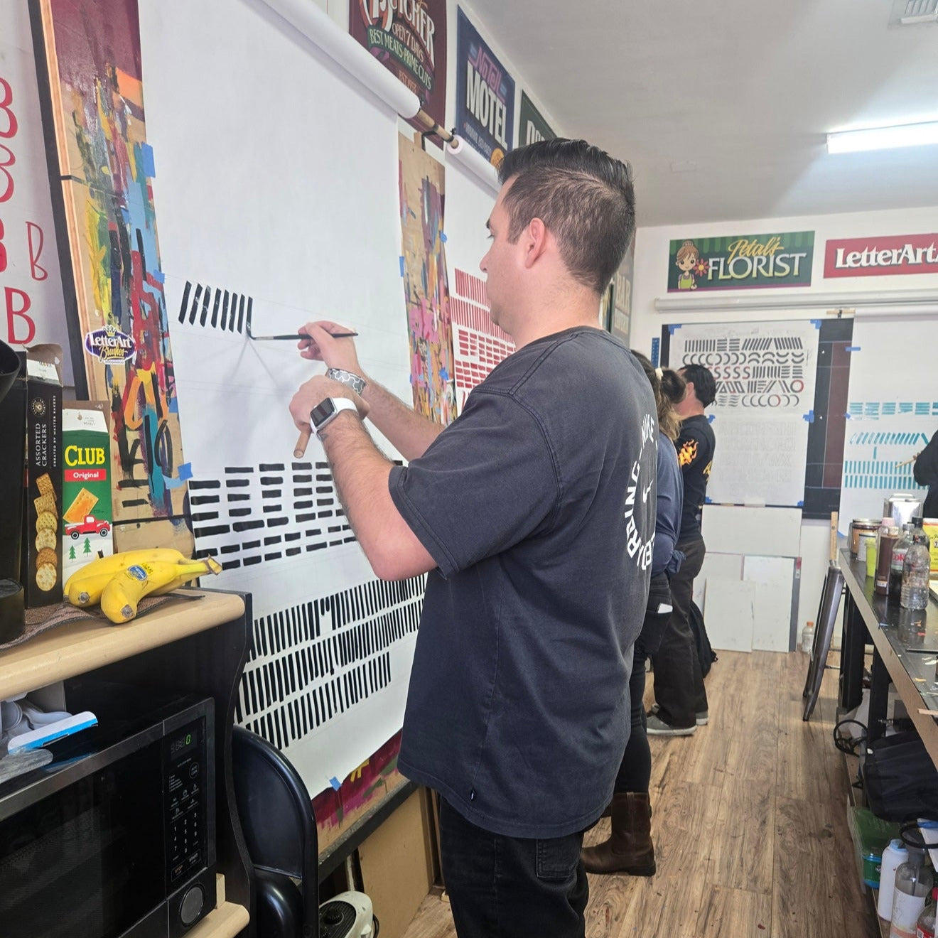 Person painting on a whiteboard in a store with various items and signs in the backgroundsign painting signwriting workshop los angeles John King